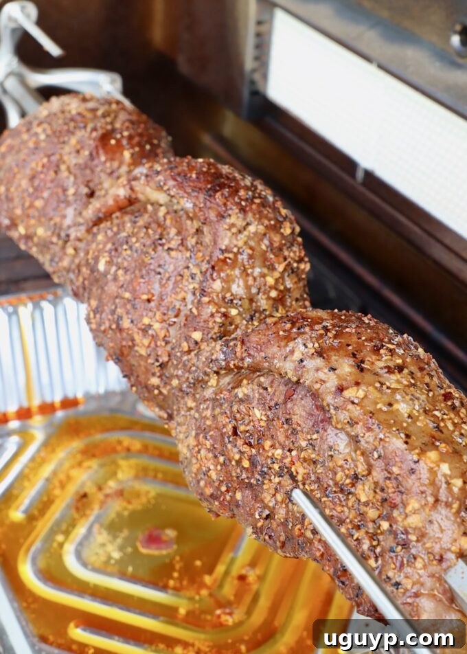 Cooked picanha steaks rotating on a rotisserie rod within an outdoor grill, with a delicious sear.