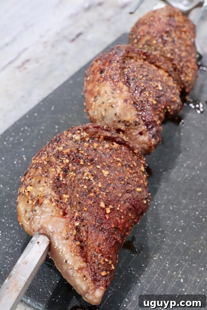 Three perfectly cooked picanha steaks still on the rotisserie rod, removed from the grill and resting on a cutting board.