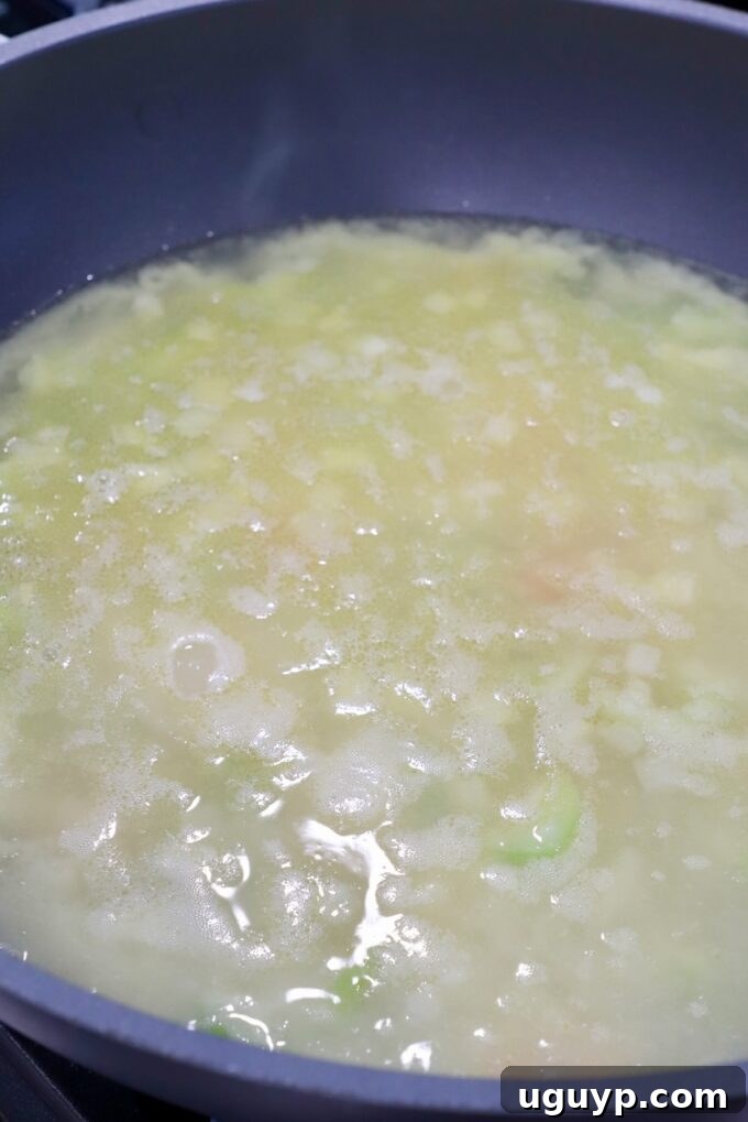 Rich chicken broth being slowly poured into a skillet with a vegetable and flour mixture