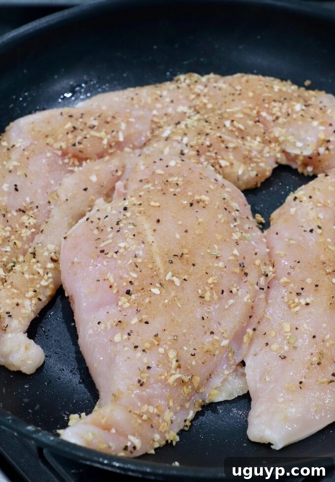 raw, seasoned chicken breasts in skillet