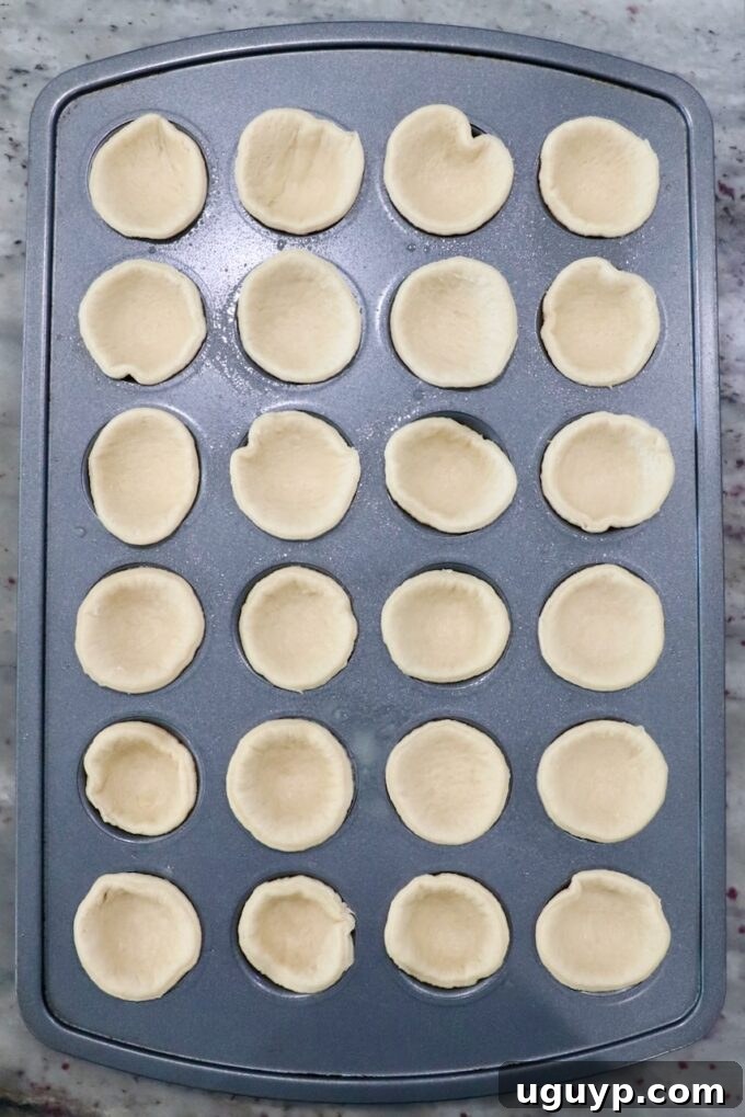 Crescent roll dough rounds gently pressed into the cups of a mini muffin tin, forming individual pie crusts.