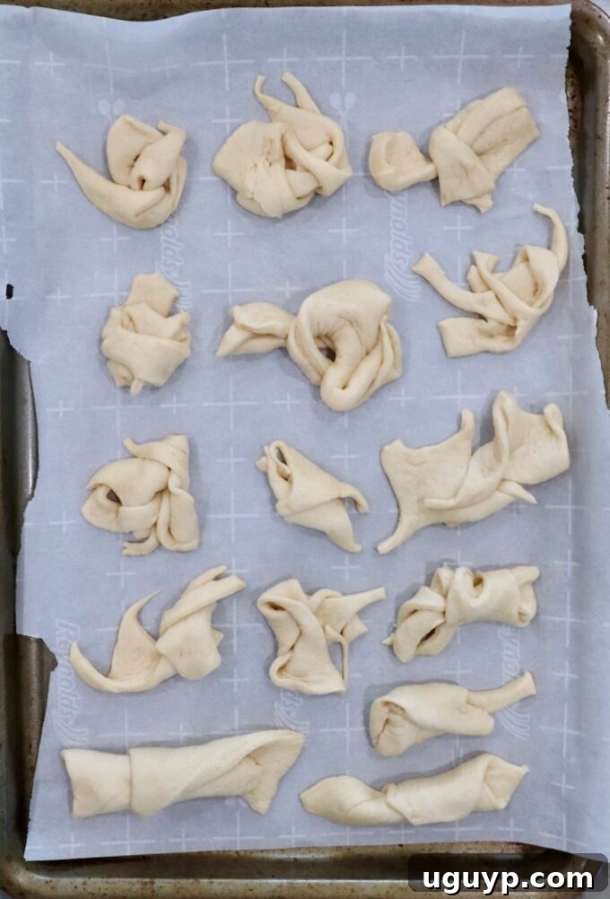 Scraps of crescent roll dough neatly tied into small knots, arranged on a parchment-lined baking sheet, ready to be baked.