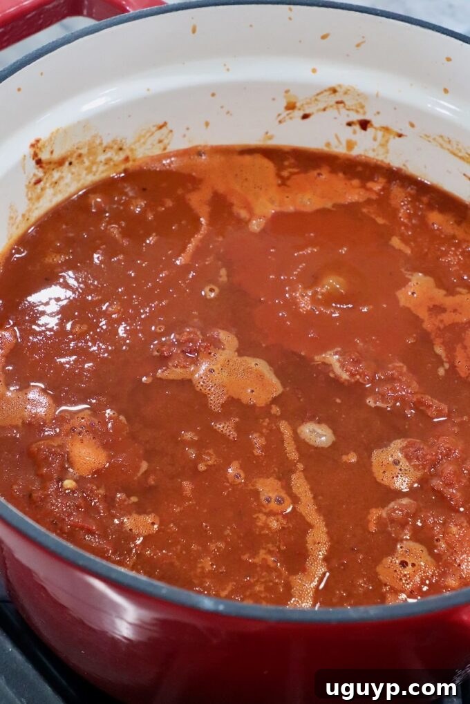 beef covered in tomato chili broth in large pot, simmering