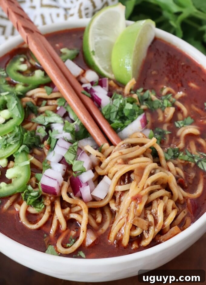 cooked ramen noodles in beef broth in bowl topped with diced onions and sliced jalapenos, a birria ramen dish
