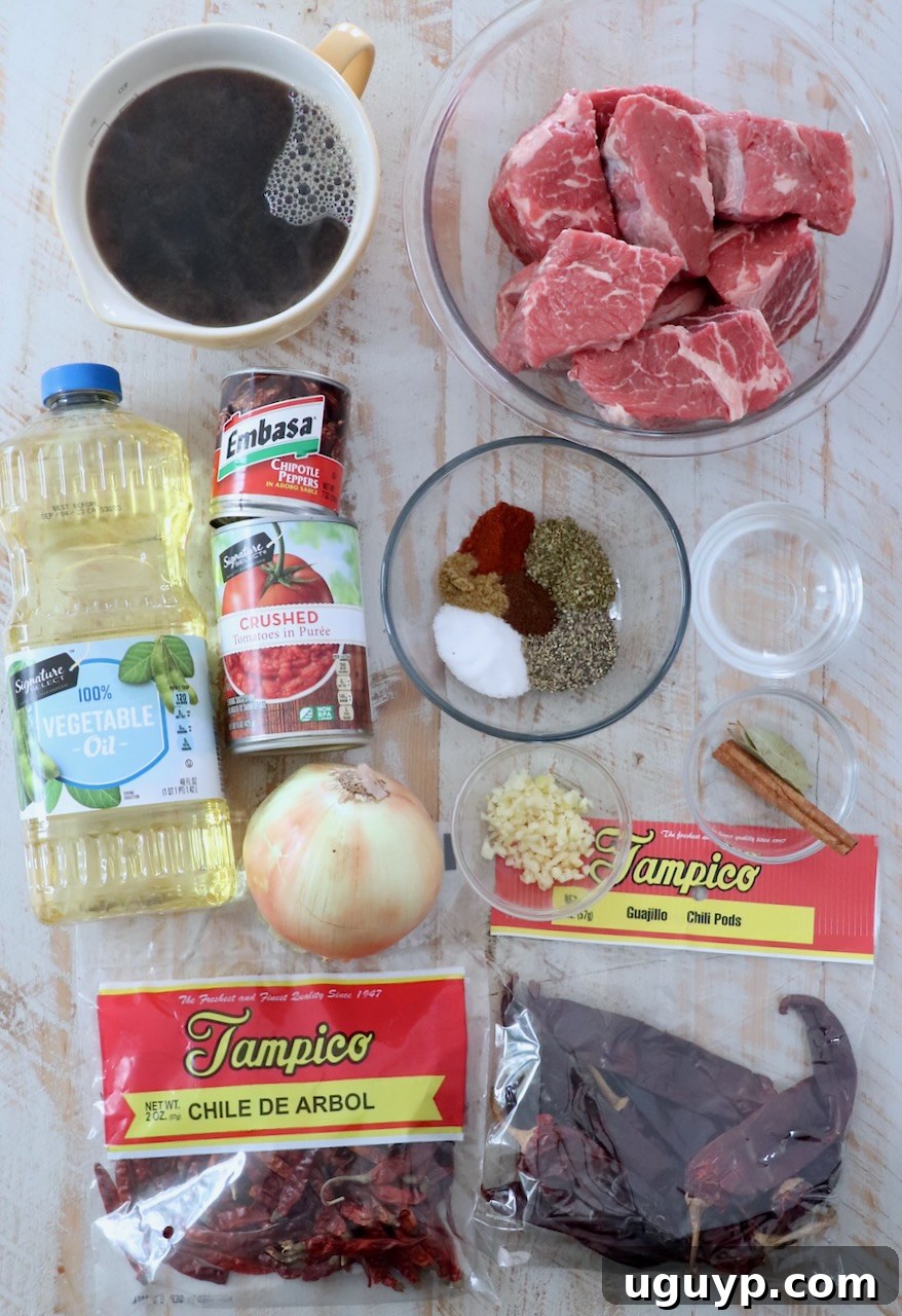ingredients for birria on white wood board, including various dried chiles, spices, and beef