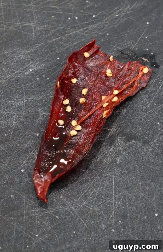dried chili pepper cut open on cutting board, showing seeds being removed