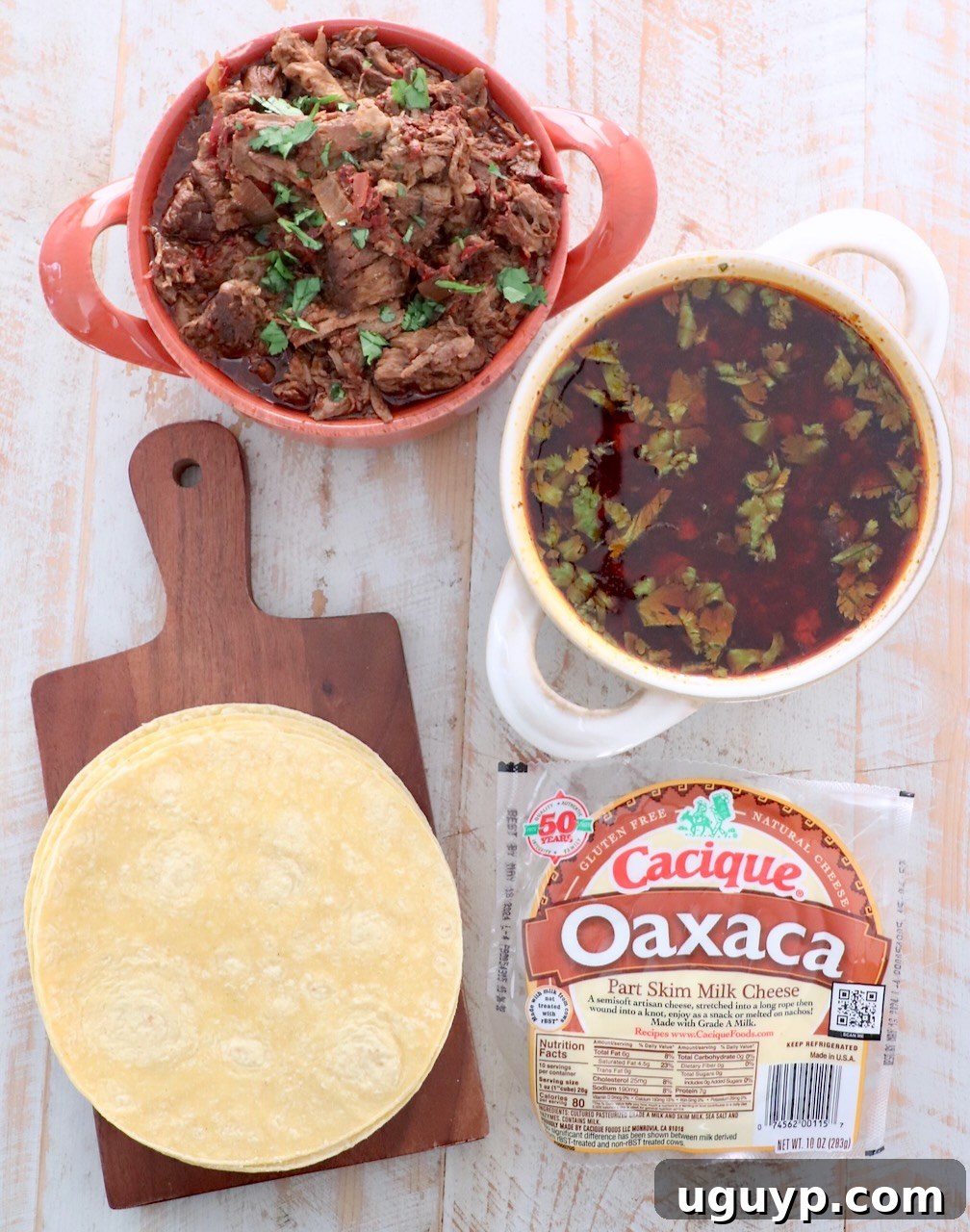 Ingredients for quesabirria tacos laid out on a white wooden board, including shredded beef birria, corn tortillas, and Oaxaca cheese.