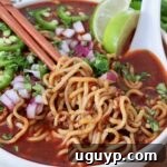 cooked ramen noodles lifted up with chopsticks in bowl of birria broth