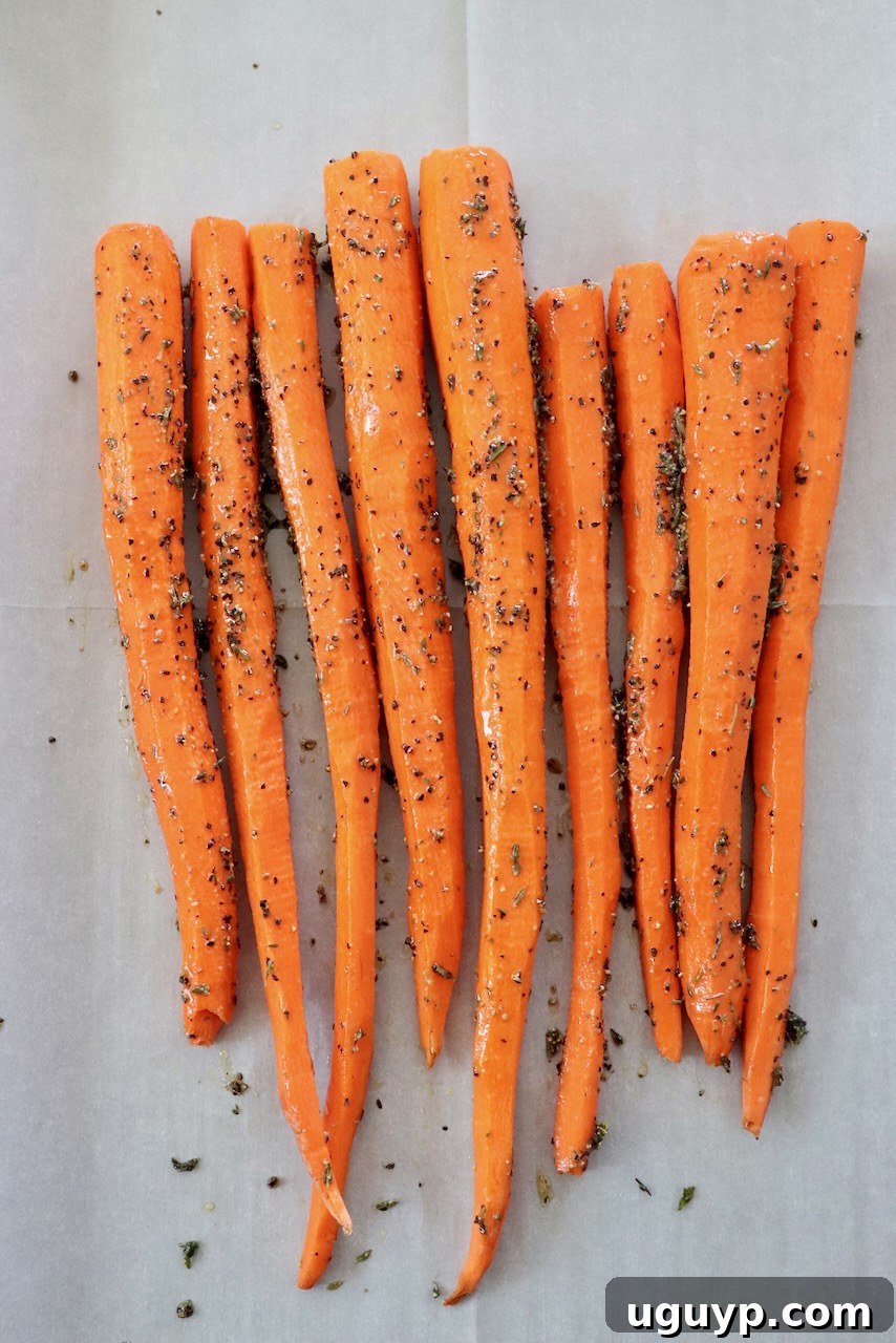 Seasoned carrots arranged in a single layer on a parchment-lined baking sheet, ready for roasting.