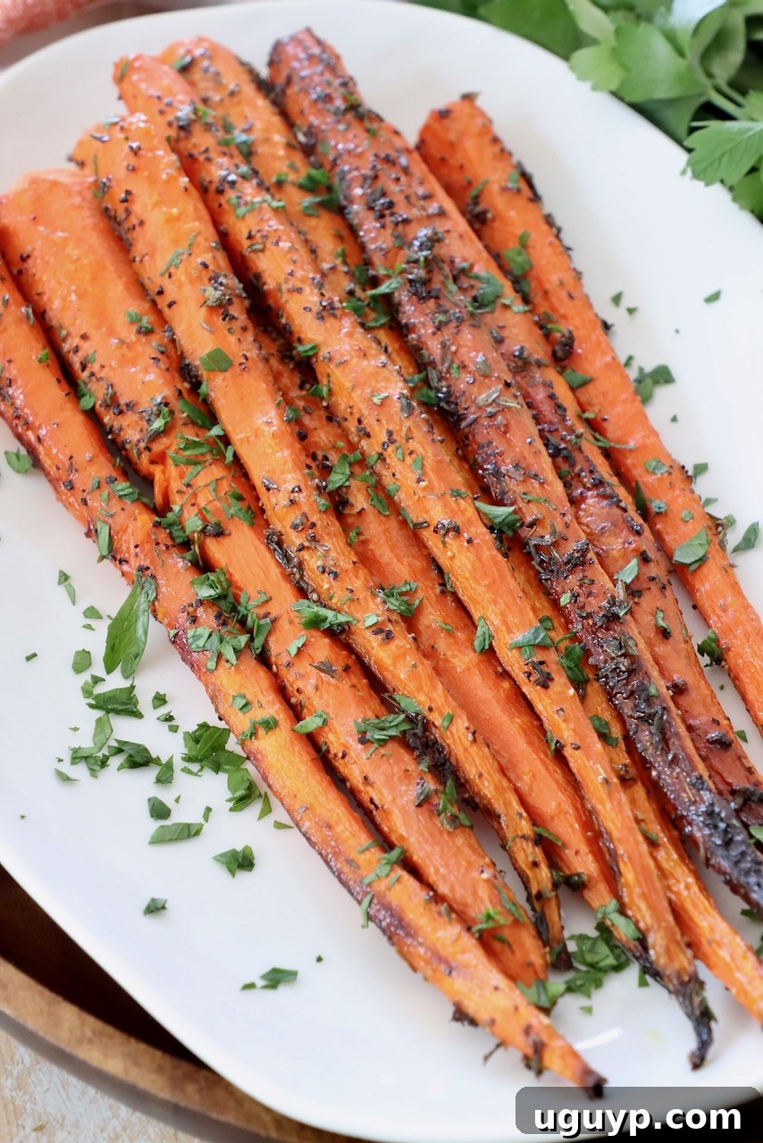 A serving of perfectly roasted carrots, glistening with olive oil and topped with fresh parsley, presented on a simple white plate.