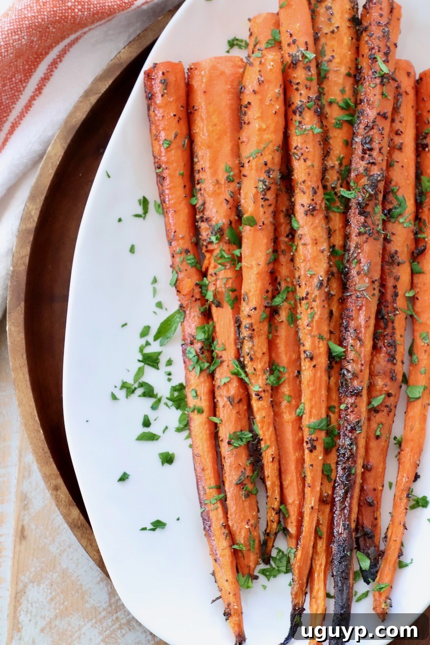 Whole roasted carrots on a white plate, elegantly garnished with fresh herbs, showcasing their rustic appeal and golden-brown finish.