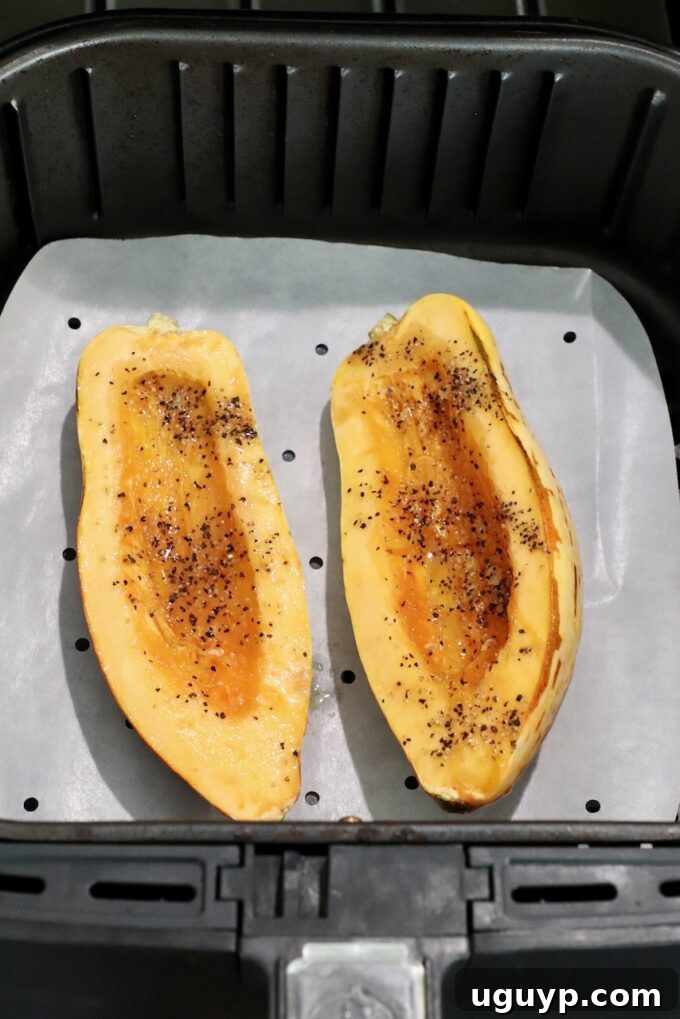 seasoned raw delicata squash sliced in half in air fryer basket