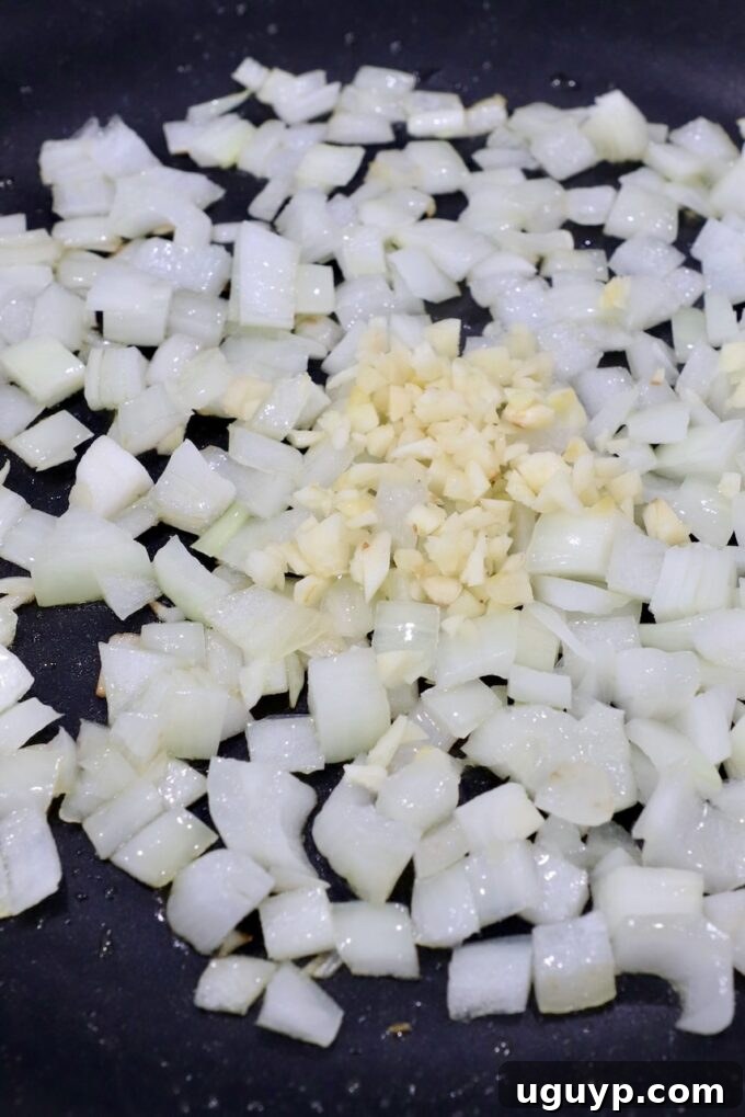 Finely diced yellow onions and freshly minced garlic cloves sizzling gently in a large skillet with olive oil, creating an aromatic base for the savory chicken sausage stuffing.