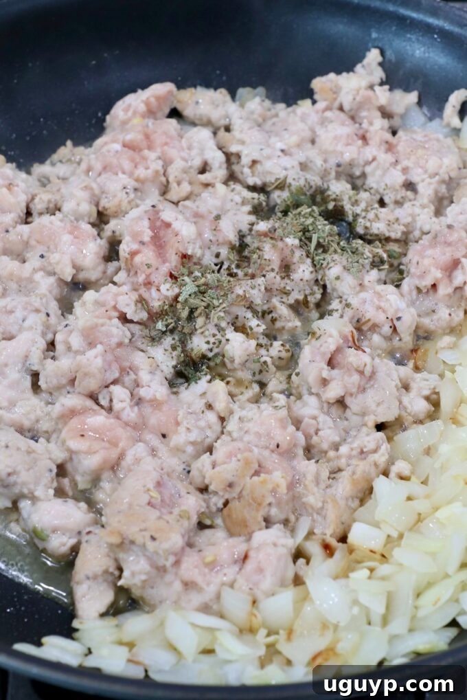 Crumbled ground chicken sausage, mixed with sautéed diced onions, minced garlic, and aromatic dried sage, cooking in a skillet until perfectly browned and fragrant, forming the hearty stuffing.