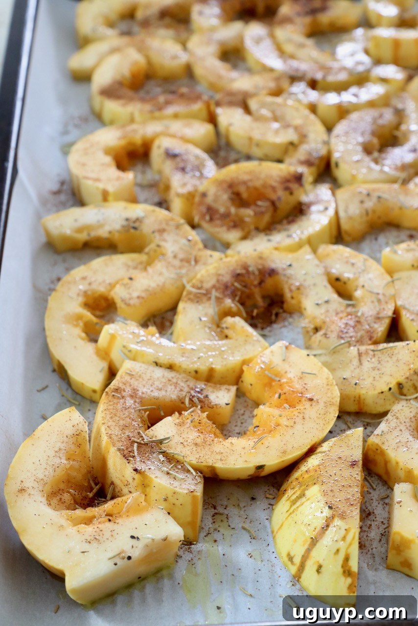 Sliced delicata squash seasoned on a baking sheet, ready for roasting