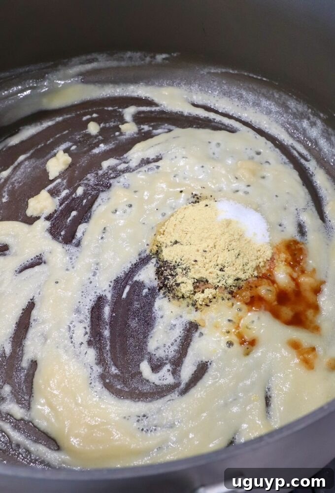 A golden roux simmering in a large pot with hot sauce and spices just added, being whisked to combine all the flavors.