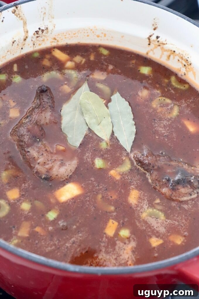 Seared short ribs immersed in a rich braising liquid of Guinness and beef stock with bay leaves, ready for the oven.
