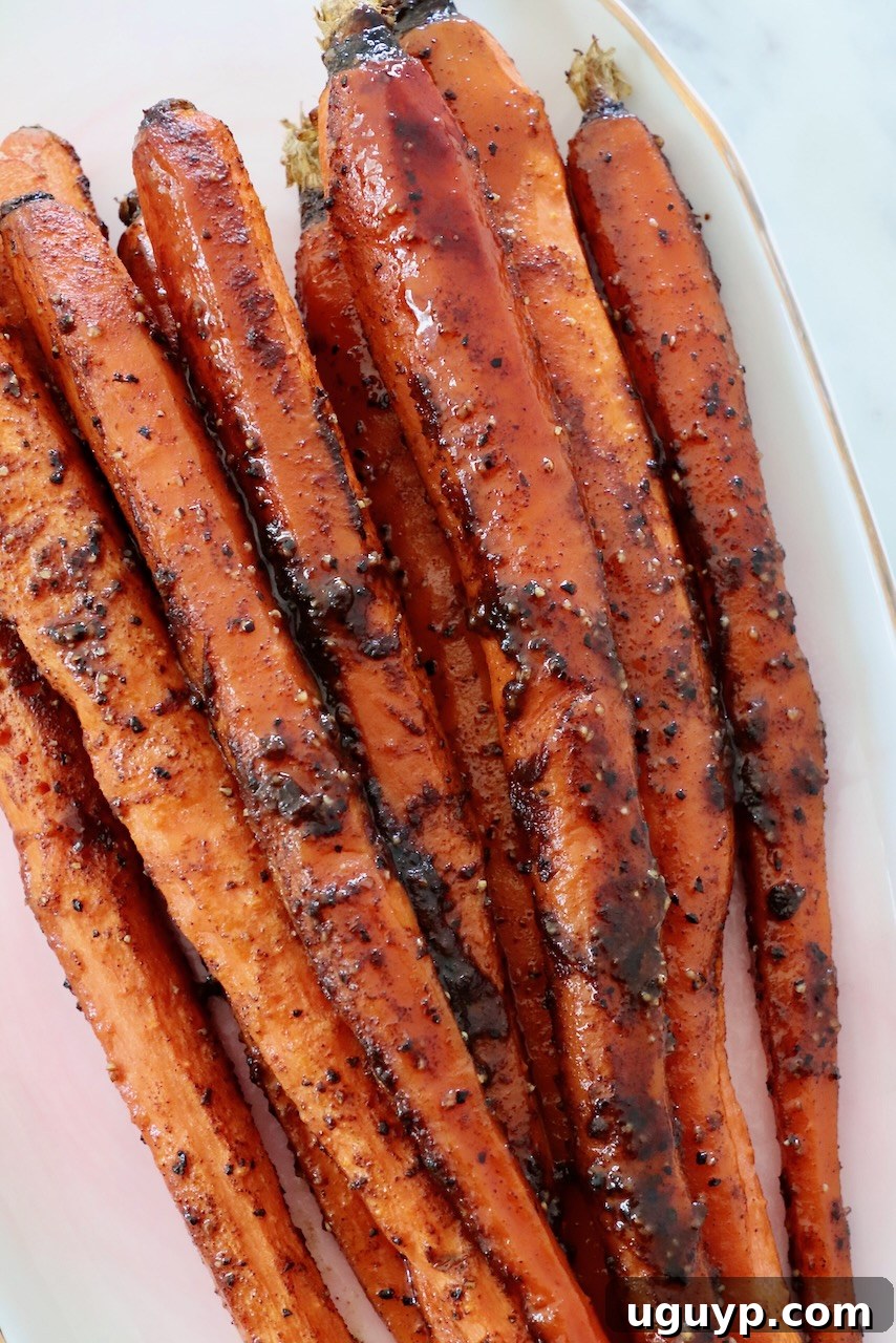 Roasted, seasoned carrots on a white plate, garnished with fresh herbs, showcasing their golden-brown glaze.