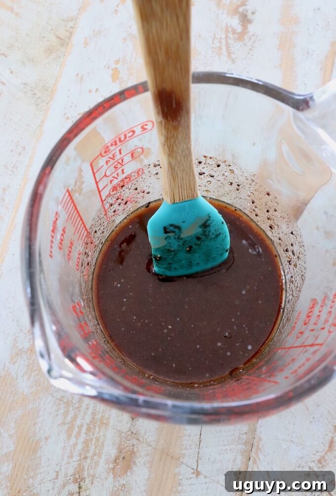 A glass measuring cup filled with a golden honey butter glaze, with a spatula resting inside.