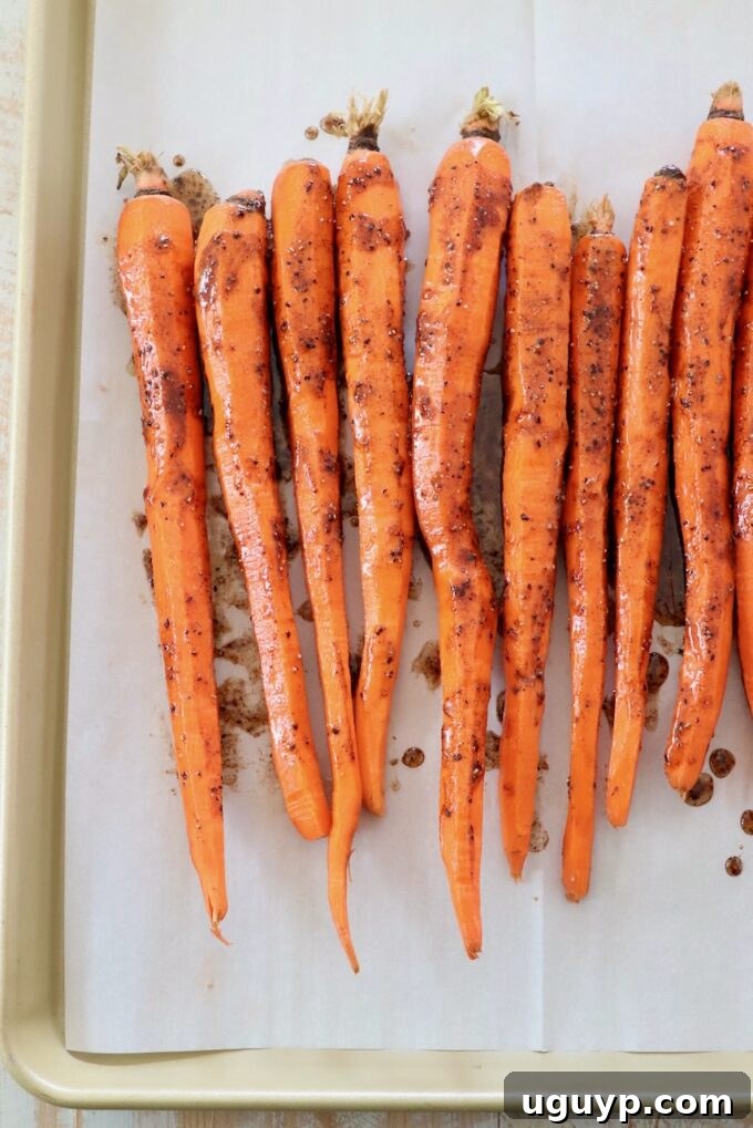 Honey glazed carrots arranged in a single layer on a parchment-lined baking sheet, ready for roasting.