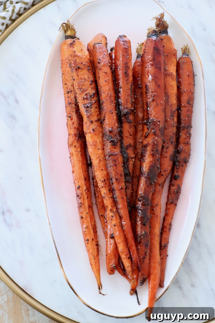Glazed roasted carrots elegantly stacked on a white plate, highlighting their appetizing sheen and tender texture.
