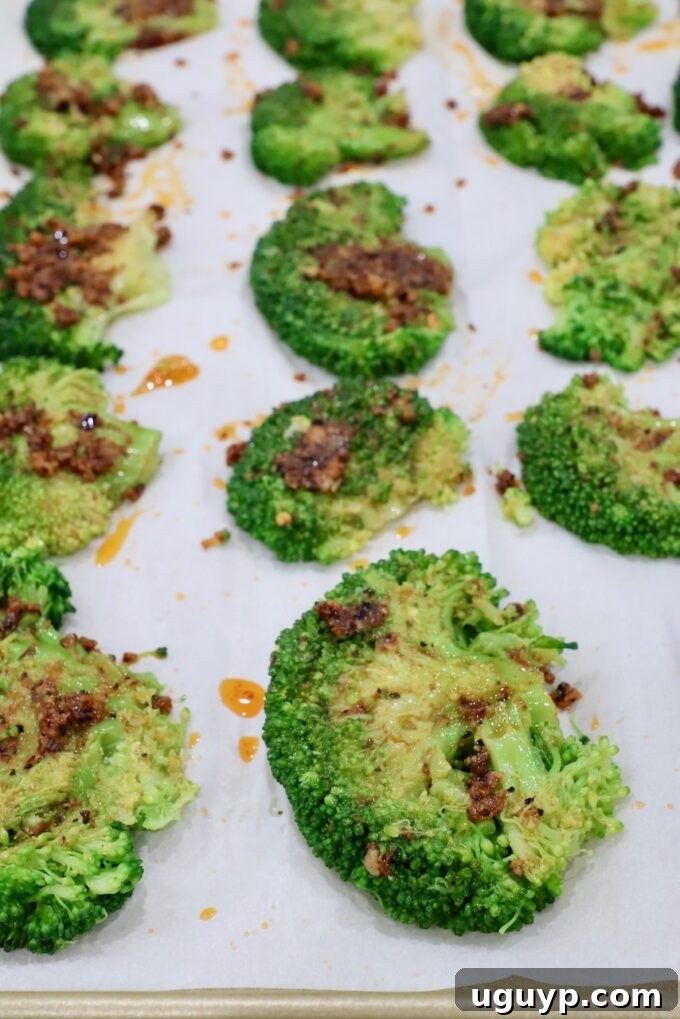 Smashed and seasoned broccoli florets arranged on a parchment-lined baking sheet