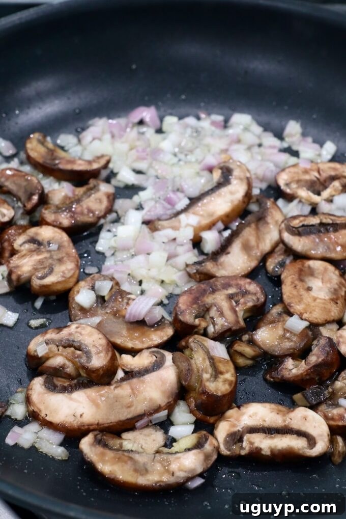 Sliced mushrooms and diced shallots sautéing in a skillet.