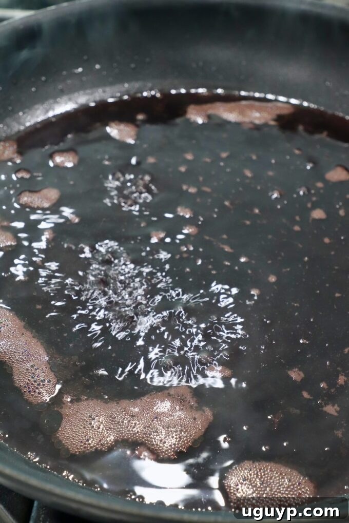 Red wine and beef broth simmering in a skillet to form a sauce base.