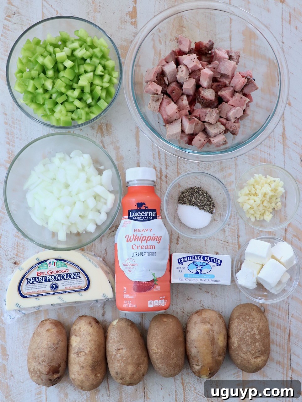 Carefully arranged ingredients for cheesesteak hash on a white wooden board, showcasing fresh produce and cheeses.
