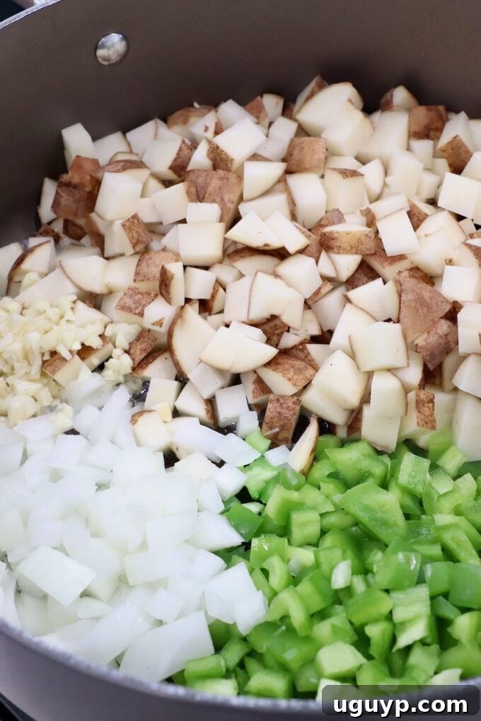 Diced potatoes, green peppers, and onions beginning to cook in a large Dutch oven.