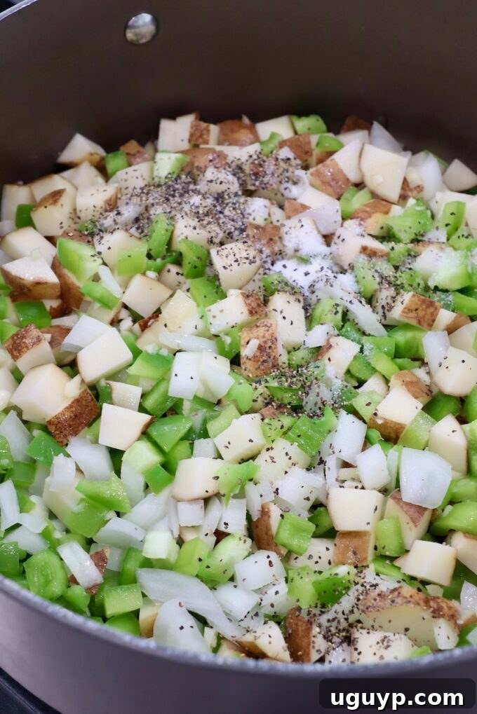 Seasoned diced potatoes and vegetables turning golden brown in a Dutch oven.