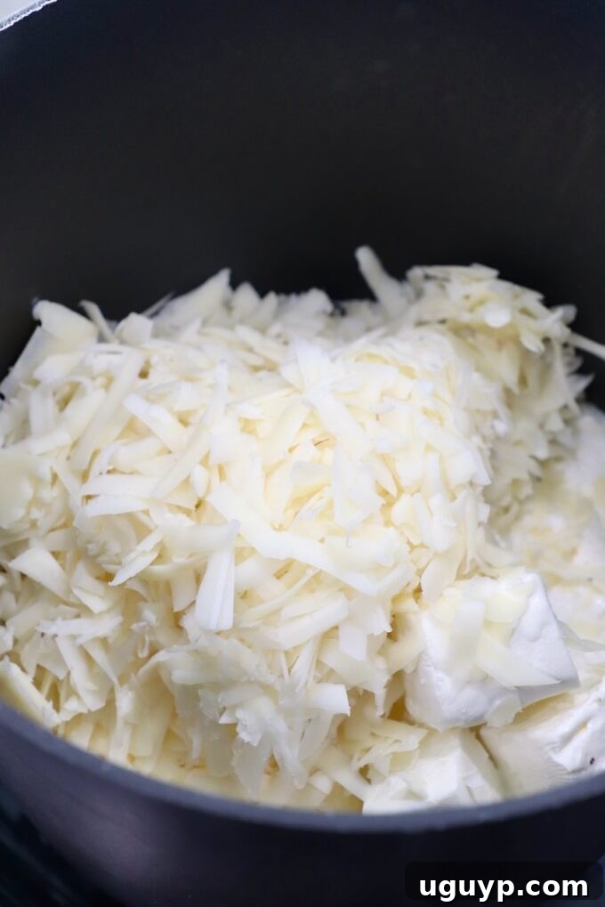 Shredded provolone and cubed cream cheese melting in a saucepan for the cheese sauce.