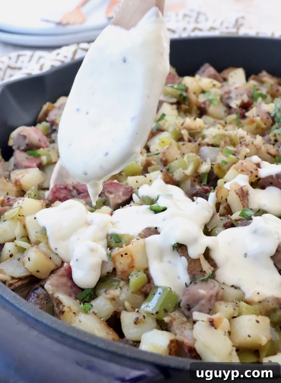 Rich, creamy cheese sauce being generously drizzled from a spoon over a skillet full of potato hash.