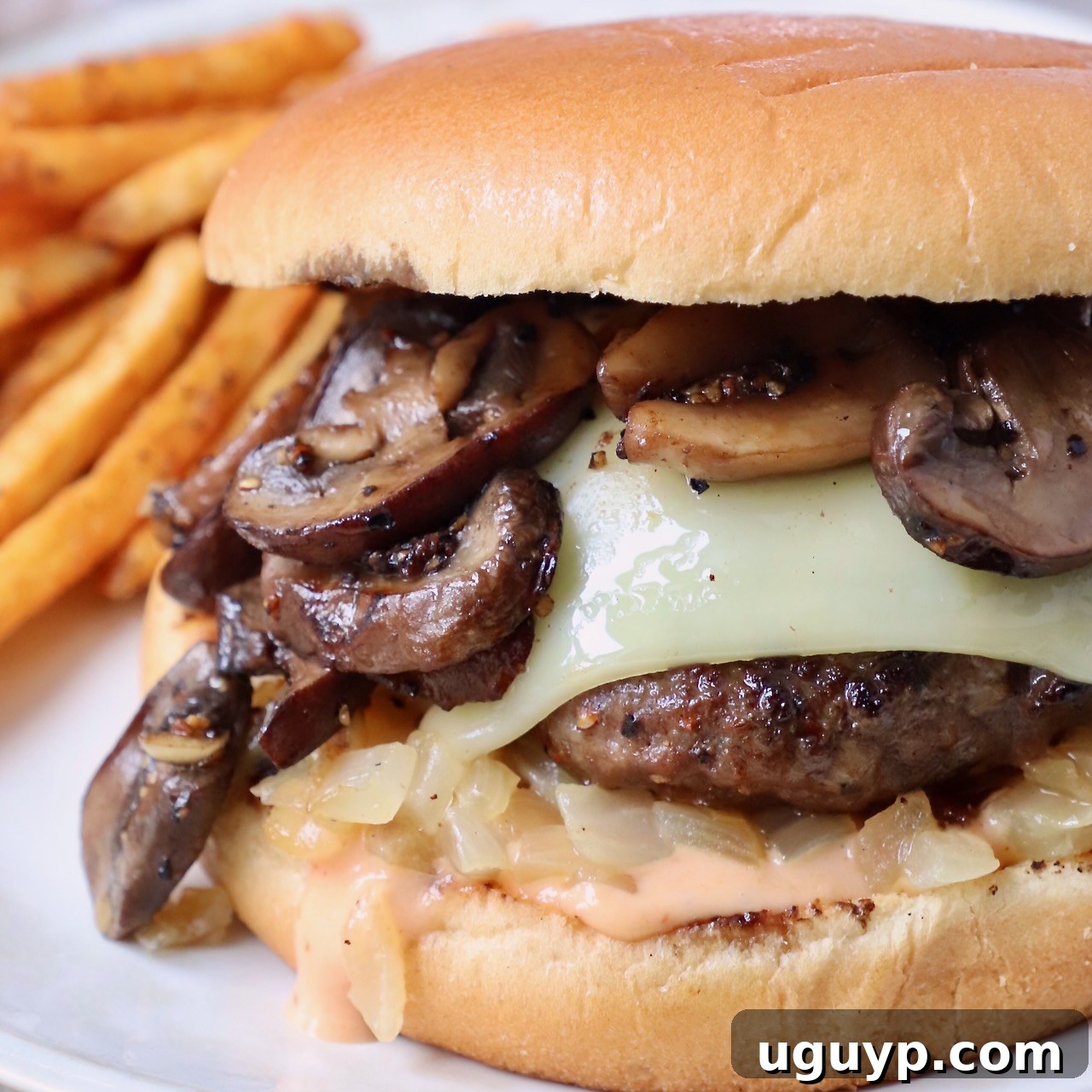 cooked cheeseburger topped with sauteed mushrooms on plate with seasoned fries