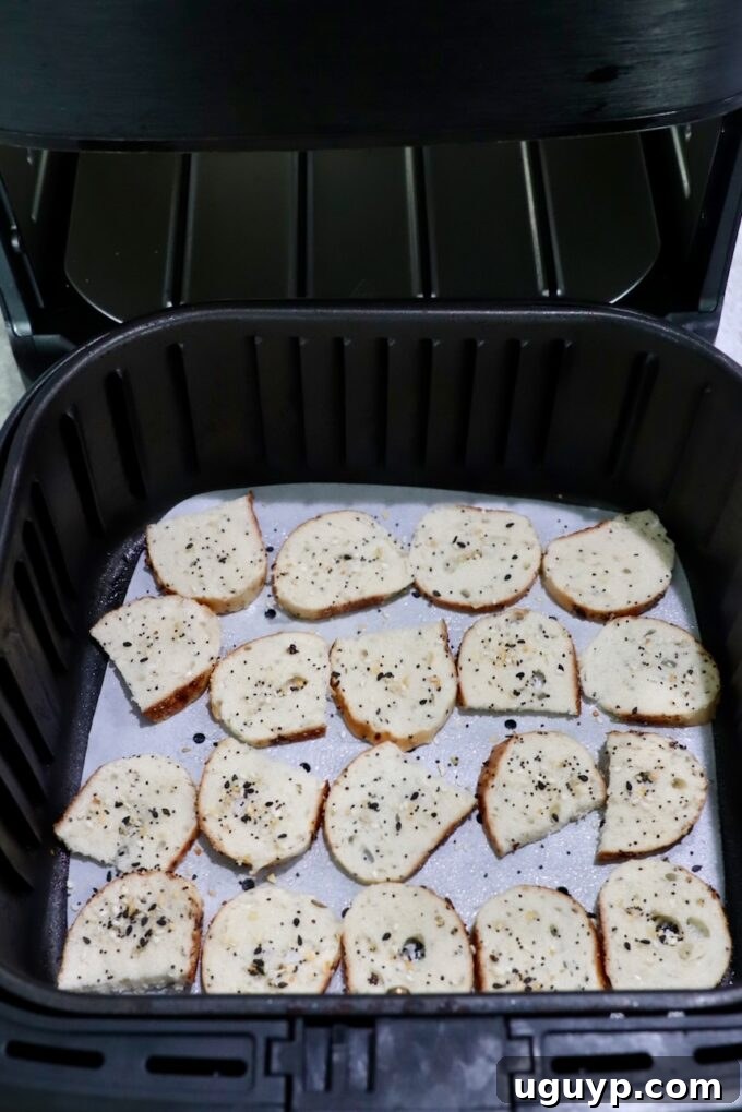 Seasoned bagel chips arranged in a single layer in an air fryer basket.