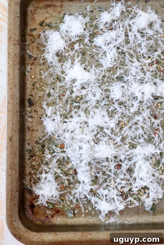 Grated Parmesan cheese and Italian seasoning layered on a baking sheet, ready for potatoes.