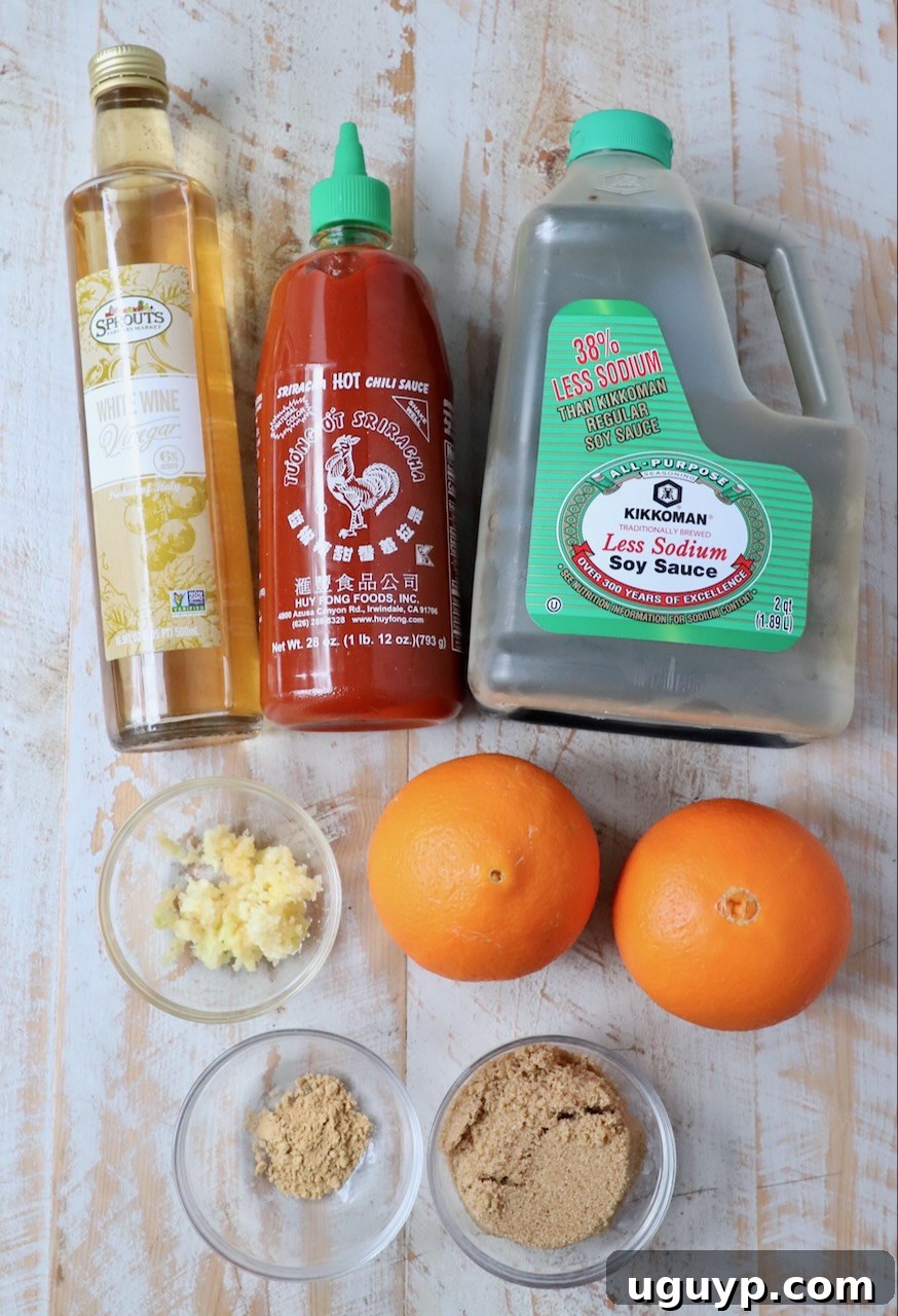 An array of fresh ingredients for Chinese orange sauce displayed on a white wooden board.