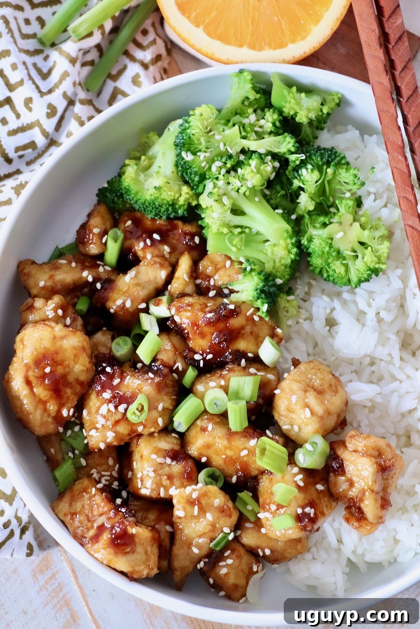 A bowl of delicious orange chicken with steamed broccoli and white rice.