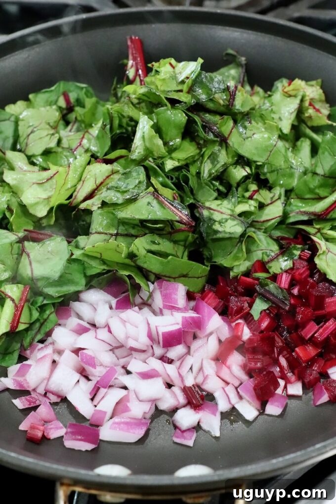 Beet greens, diced beet stems, and diced onions in a skillet, ready for the egg mixture.