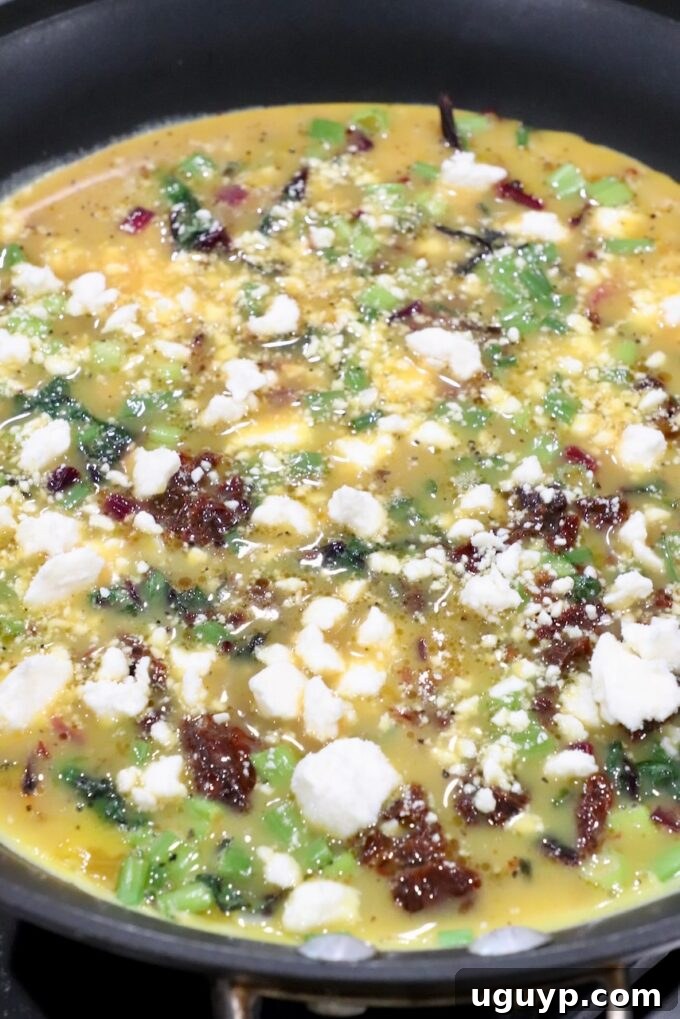 Uncooked frittata in a skillet, generously topped with crumbled feta cheese before baking.