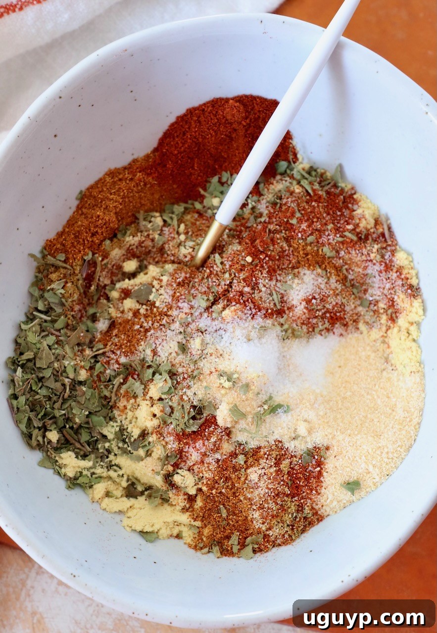 Assortment of spices and dried herbs meticulously mixed in a bowl, with a spoon ready for use.