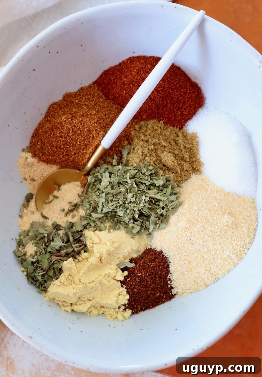 Distinct dried herbs and spices elegantly separated in a bowl, with a spoon nestled beside them, showcasing the components of the blend.