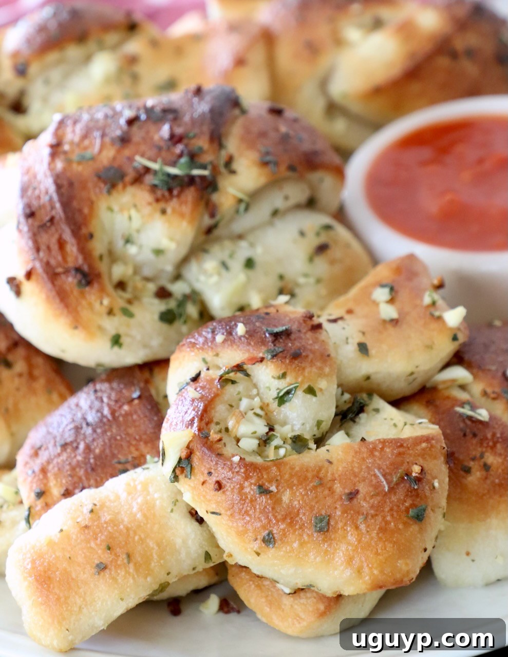 Freshly baked garlic knots on a plate, served with a small bowl of marinara sauce for dipping.