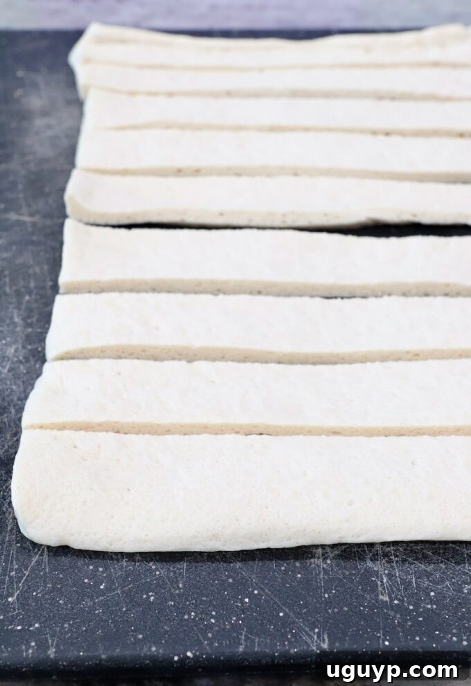 Sliced pizza dough strips on a cutting board, ready to be tied into knots.
