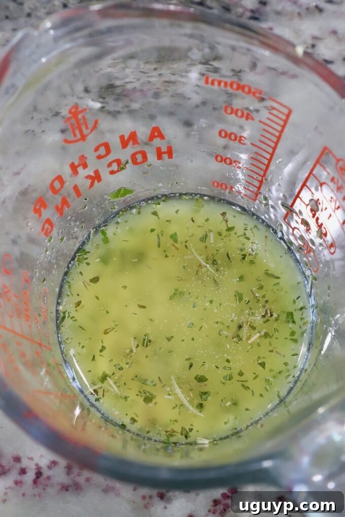 Seasoned melted butter with crushed garlic and Italian herbs in a clear glass jar.