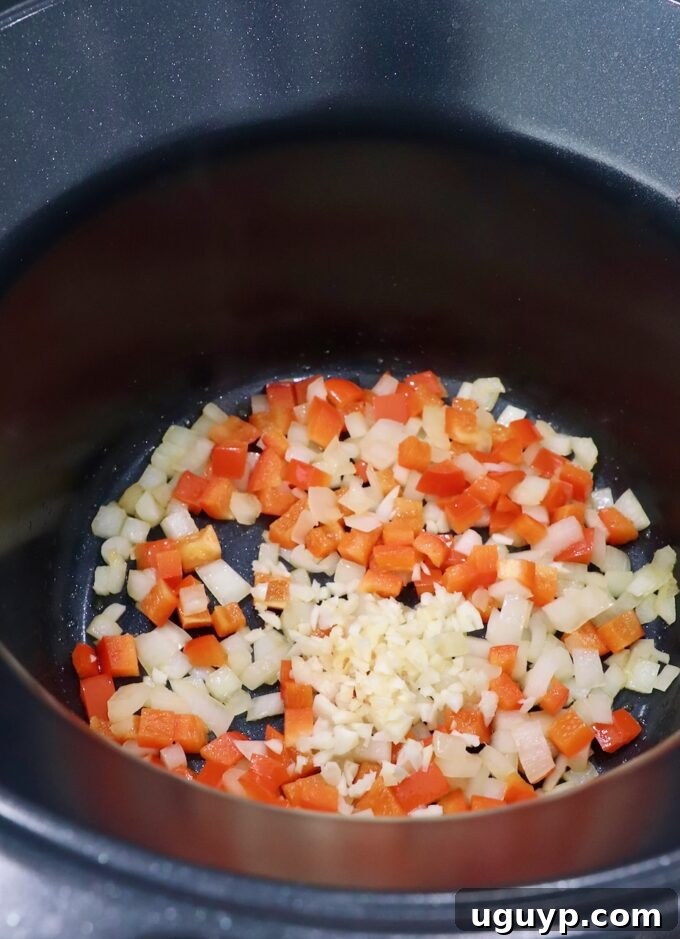 Diced red bell pepper, onion, and minced garlic being sautéed in a pot on the stove.