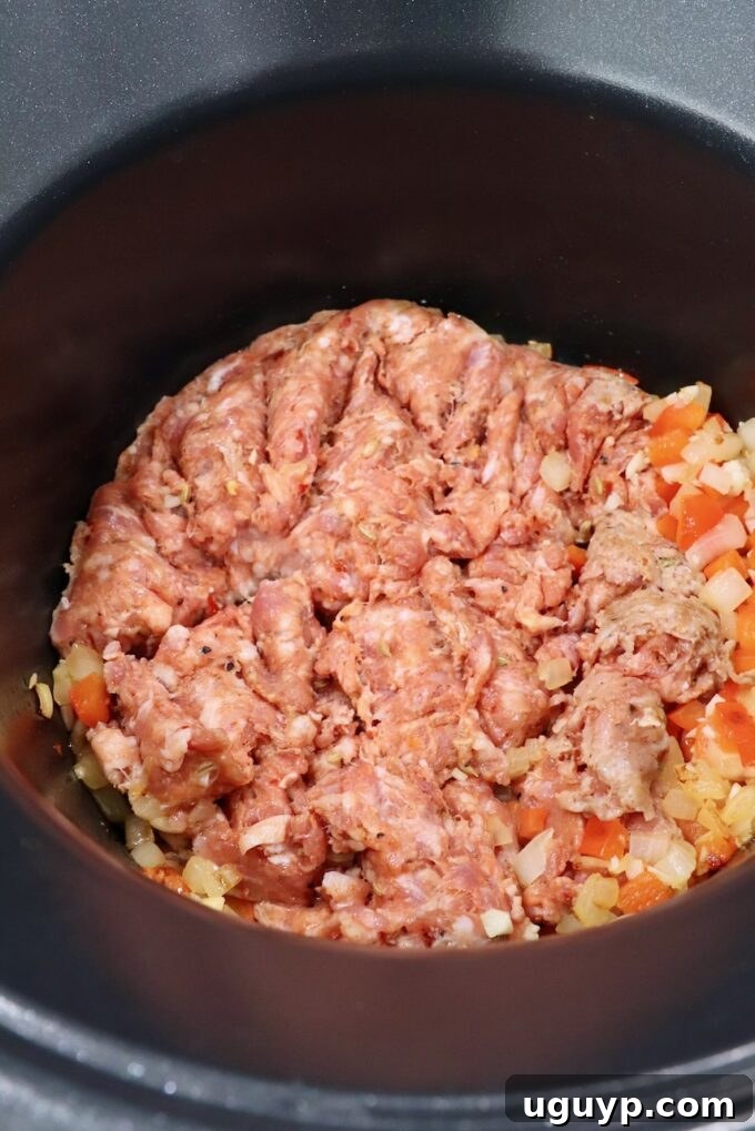 Loose Italian sausage browning in a pot with diced vegetables.