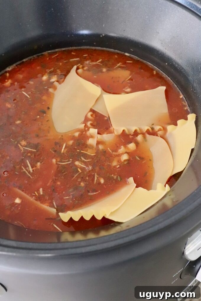 Broken lasagna noodles added to the tomato sauce mixture in a slow cooker.