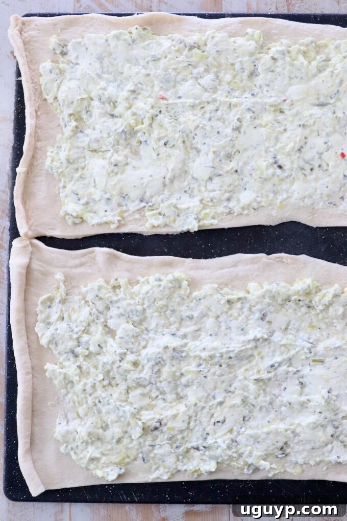 The creamy dill pickle mixture evenly spread across a sheet of crescent roll dough on a cutting board.