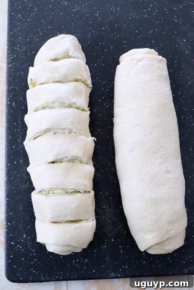 A tightly rolled log of crescent dough filled with the creamy pickle mixture, being sliced into individual rolls with a serrated knife.